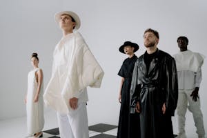 Group of models in avant-garde fashion poses in a minimalist studio setting.