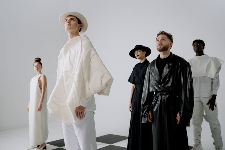Group of models in avant-garde fashion poses in a minimalist studio setting.