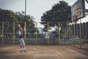 A man in athletic wear leaps for a basketball shot on an outdoor urban court.