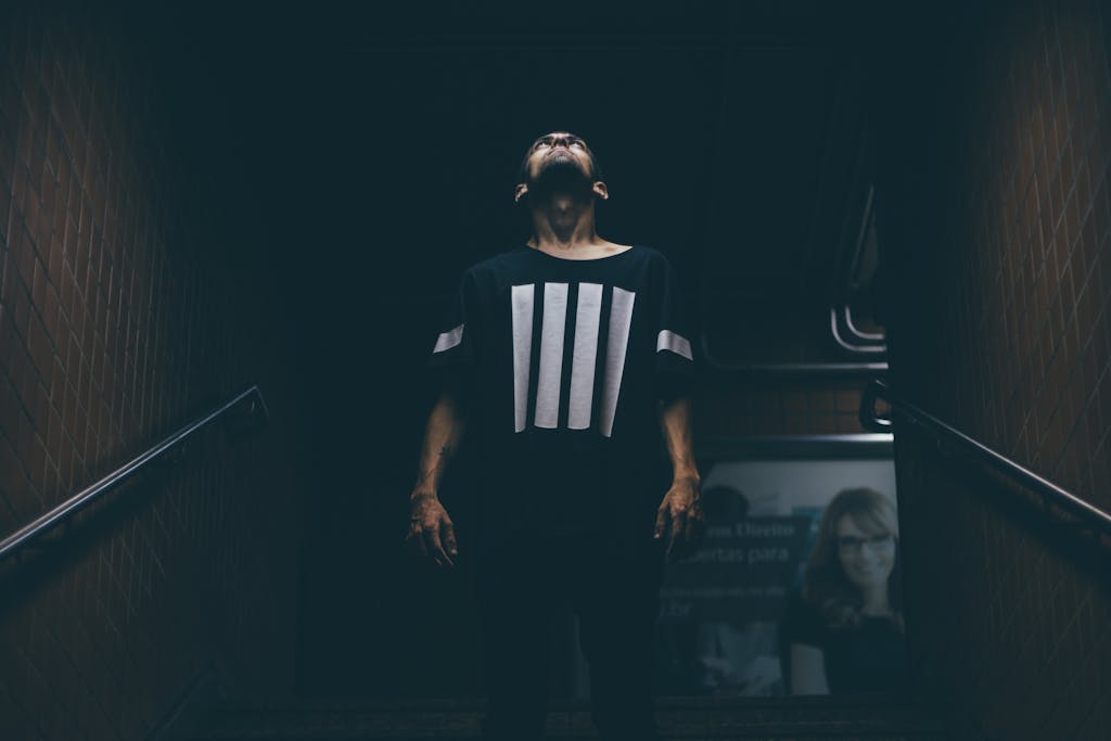 A young man stands in a dimly lit subway, looking upwards with a dramatic pose.